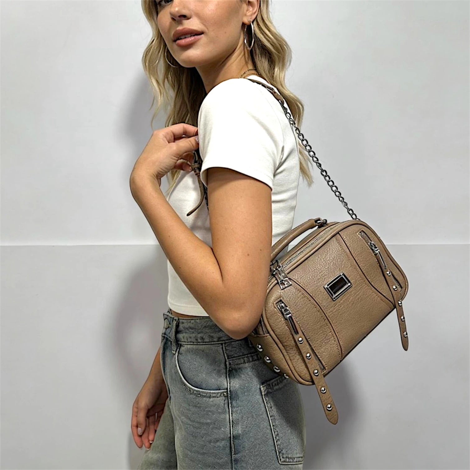 artera de diseño rectangular estructurado con múltiples cierres frontales decorativos. Incluye detalles de tachas plateadas en los laterales, doble compartimento superior y una correa mixta de cuero sintético con cadena metálica.