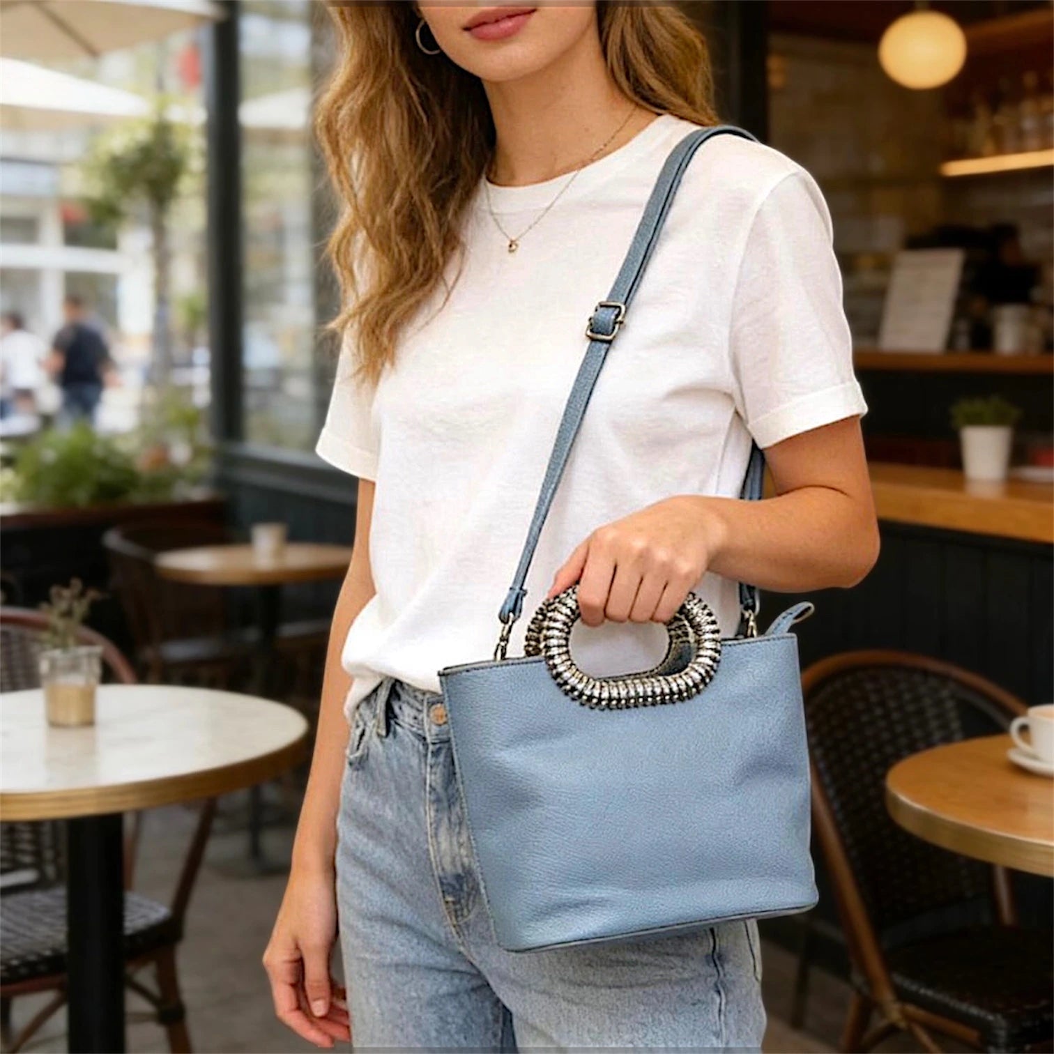 Bolso de mano estructurado de silueta tipo tote con acabado liso. Destaca por su manilla superior ovalada recubierta de cristales brillantes y una correa de hombro delgada, ajustable y removible a tono.