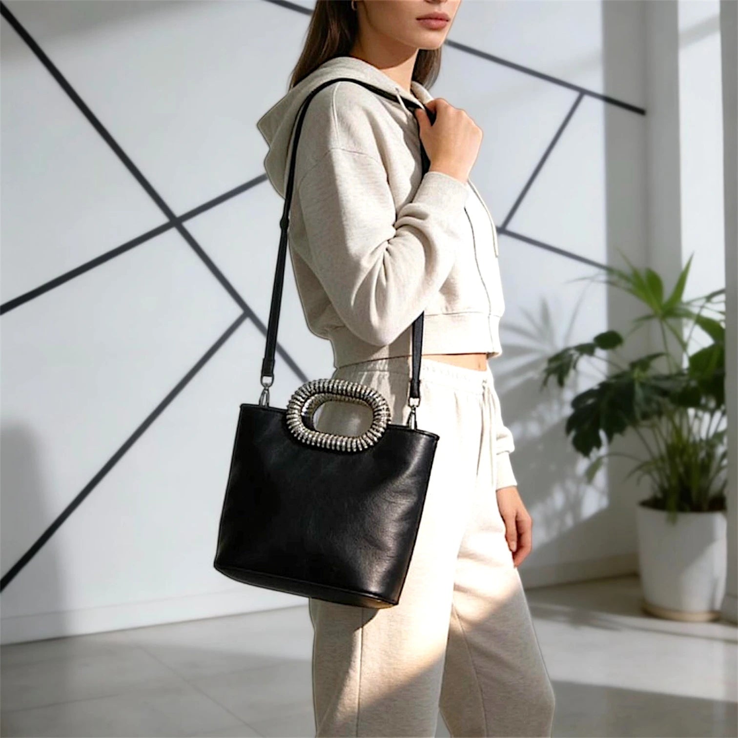 Bolso de mano estructurado de silueta tipo tote con acabado liso. Destaca por su manilla superior ovalada recubierta de cristales brillantes y una correa de hombro delgada, ajustable y removible a tono.