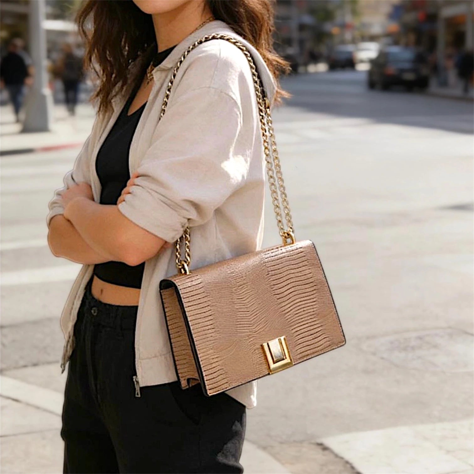 Cartera de hombro estructurada con solapa frontal en textura de piel de lagarto (lizard). Presenta un cierre metálico dorado rectangular, correa de cadena dorada entrelazada y un diseño compacto de líneas limpias.