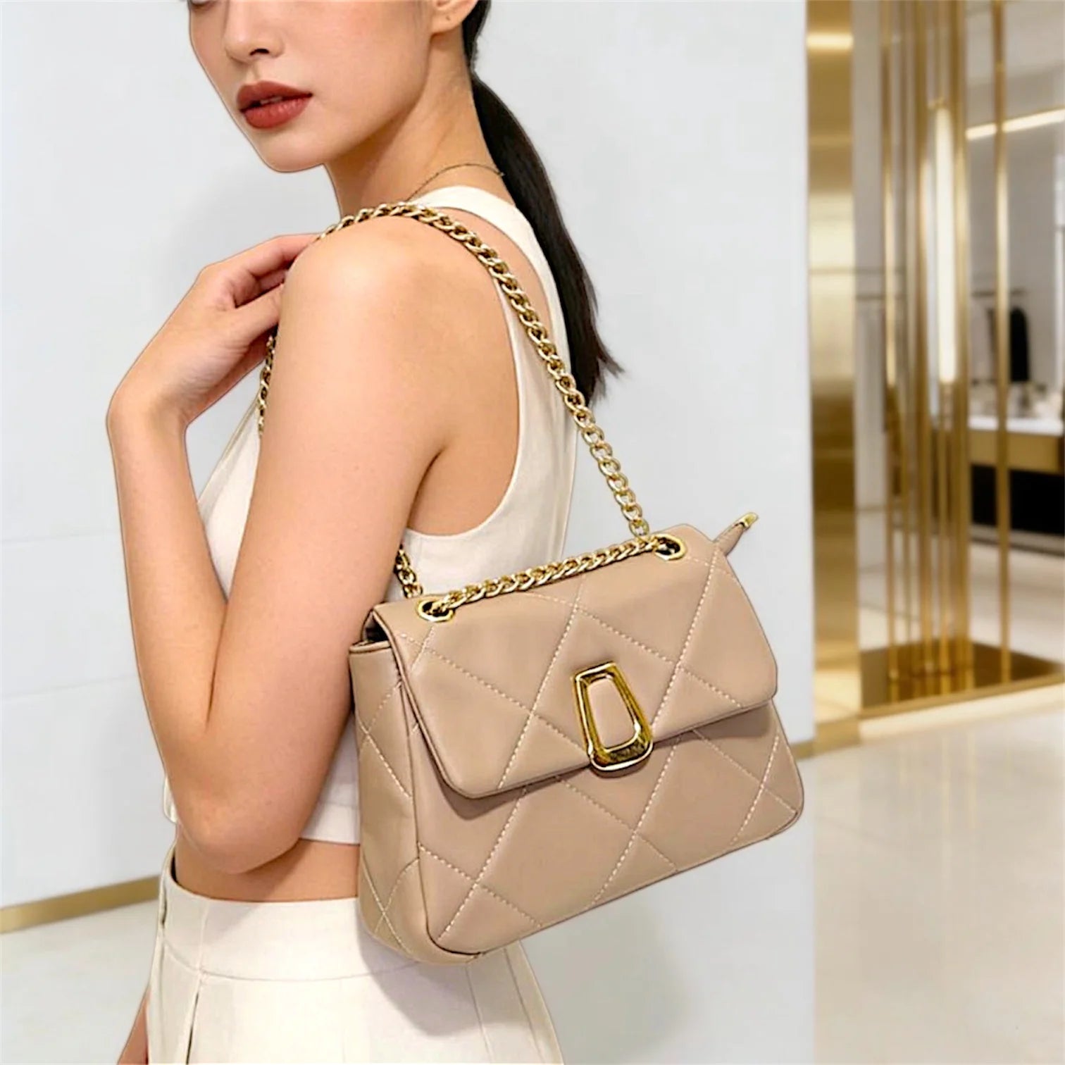 Cartera de hombro estructurada con diseño acolchado de rombos de gran tamaño (maxi quilting). Incluye una solapa frontal con cierre metálico dorado de diseño único y una correa de cadena dorada entrelazada que pasa por ojales metálicos superiores.