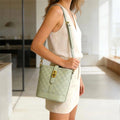 Bolso tipo bucket con textura de patrón tejido geométrico y cierre metálico dorado, diseño estilo bandolera color verde