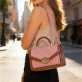 Bolso de mano estructurado con textura de rayas verticales, asa superior trenzada y distintivo broche dorado en forma de abanico en color rosa