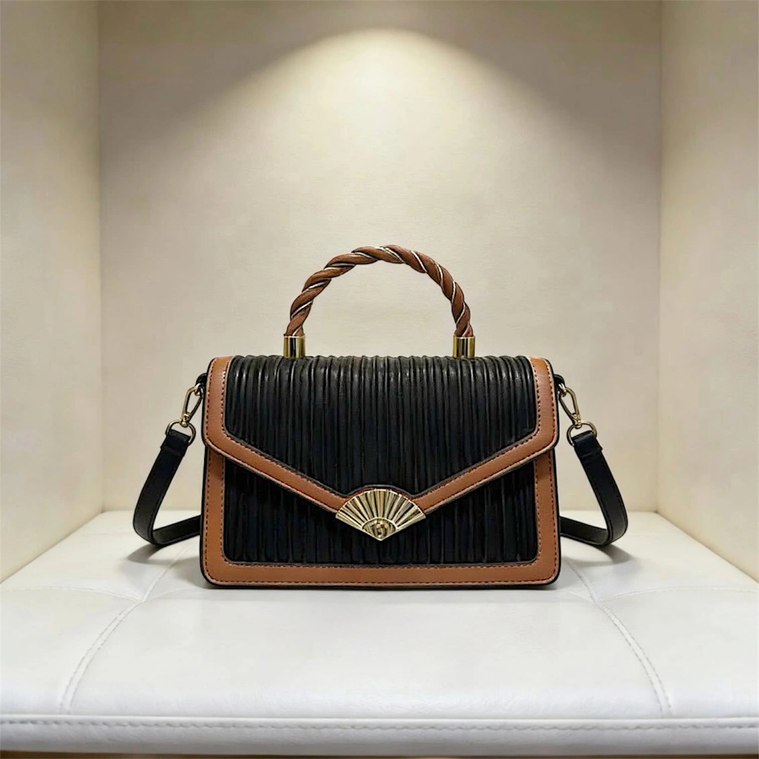 Bolso de mano estructurado con textura de rayas verticales, asa superior trenzada y distintivo broche dorado en forma de abanico en color negro