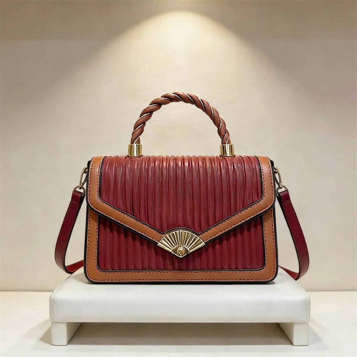 Bolso de mano estructurado con textura de rayas verticales, asa superior trenzada y distintivo broche dorado en forma de abanico en color rojo