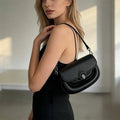 Bolso de hombro pequeño en color negro con silueta redondeada y cierre metálico circular distintivo en color negro