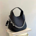 Bolso tipo hobo de color negro con textura granulada, decorado con una cadena plateada distintiva y detalles en forma de media luna