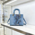 Bolso de mano estructurado con textura de piel de serpiente en tonos verdosos, asa superior y charm decorativo a juego