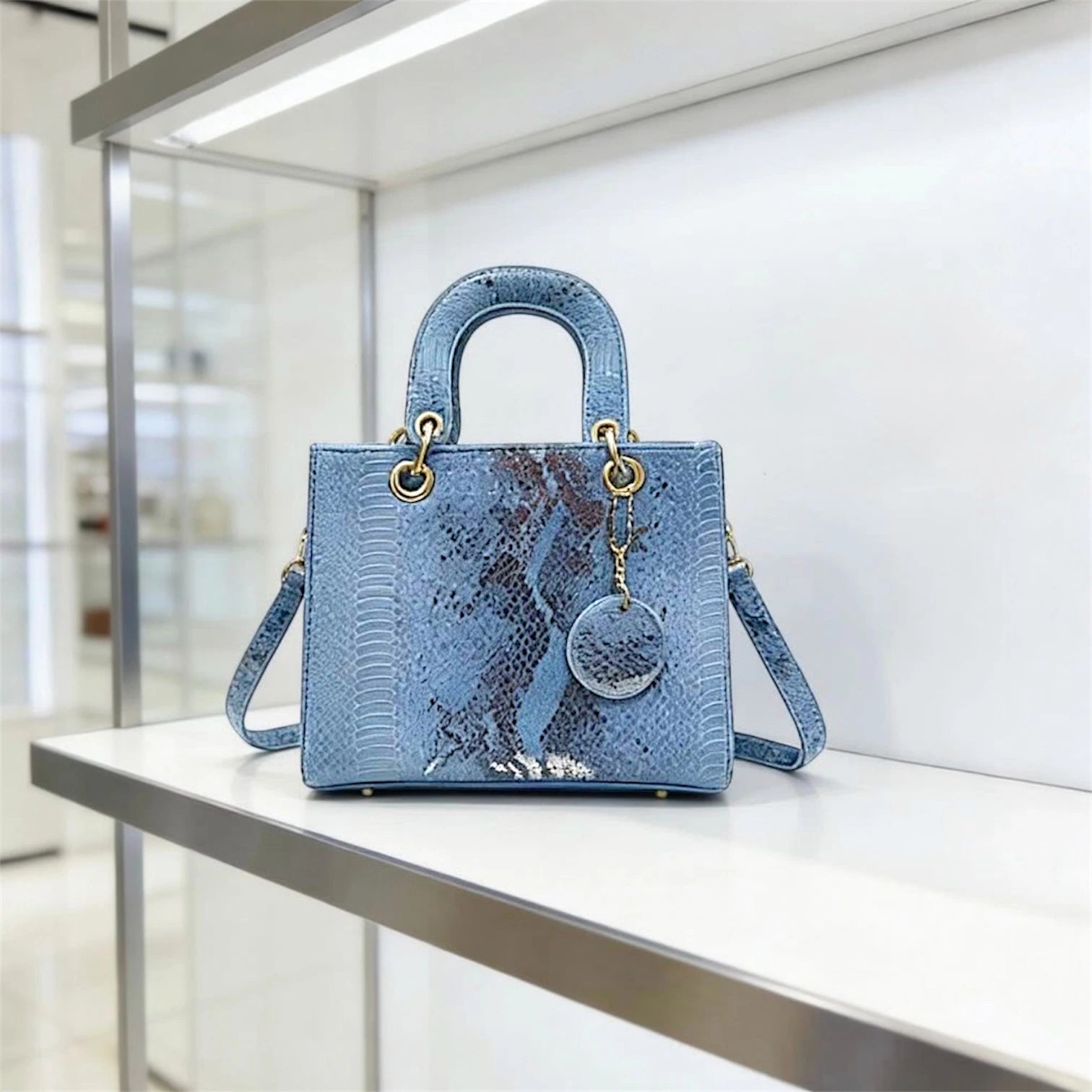 Bolso de mano estructurado con textura de piel de serpiente en tonos verdosos, asa superior y charm decorativo a juego