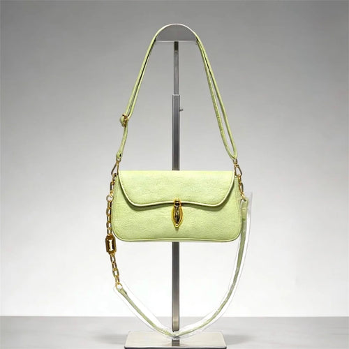 Bolso bandolera de gamuza en tono verde pálido con broche dorado ovalado distintivo y correa de cadena, estilo sofisticado y minimalista.