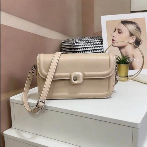 Bolso tipo bandolera de diseño minimalista con estructura redondeada y cierre circular central distintivo