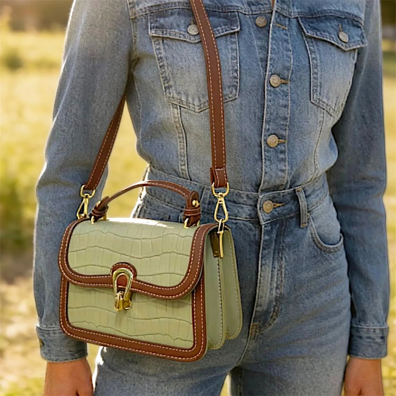 Bolso de hombro con textura de cocodrilo, costuras decorativas en contraste y cierre metálico dorado.