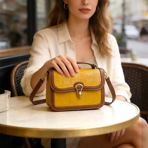 Bolso de hombro con textura de cocodrilo, costuras decorativas en contraste y cierre metálico dorado.